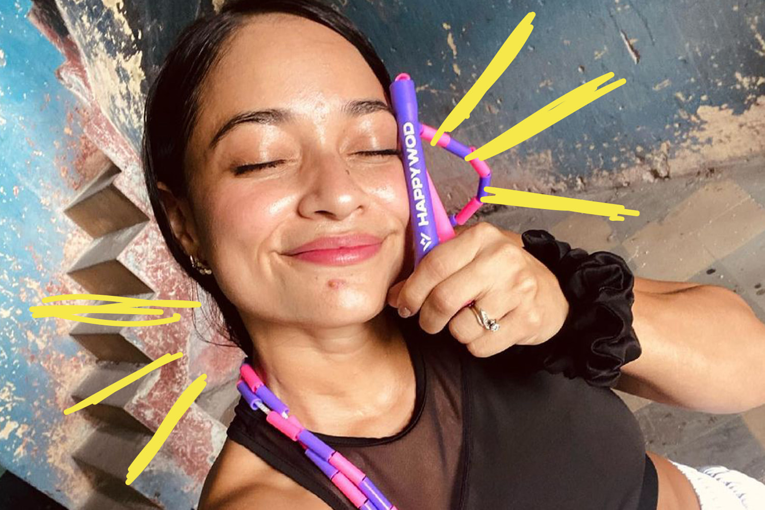 Close up of smiling woman holding handle of HappyWOD beaded jump rope to side of her face