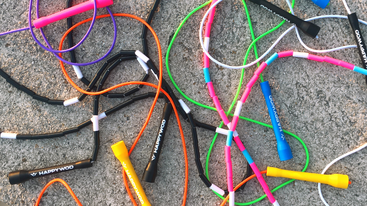 Several colorful beaded and speed jump ropes scattered on street pavement with the HappyWOD logo printed on the handle